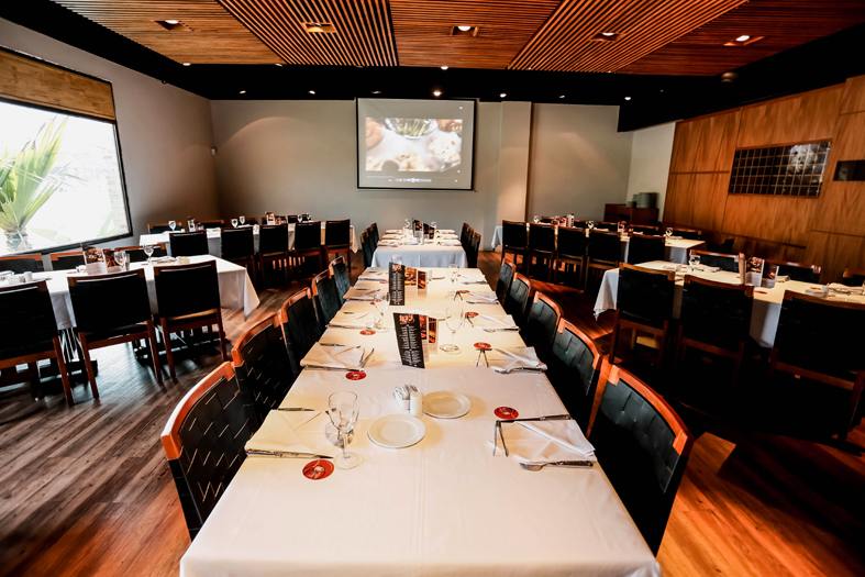 Salão do restaurante montado para evento, com mesas compridas e telão ao fundo